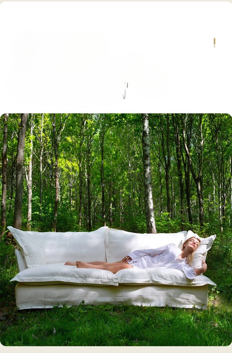 White sofa in a forest setting with a person lying on it.