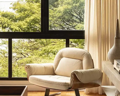 Beige armchair in a room with large windows showing greenery outside.