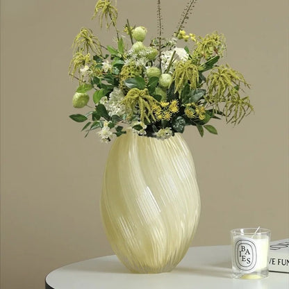 Decorative vase with green floral arrangement on a table against a beige wall