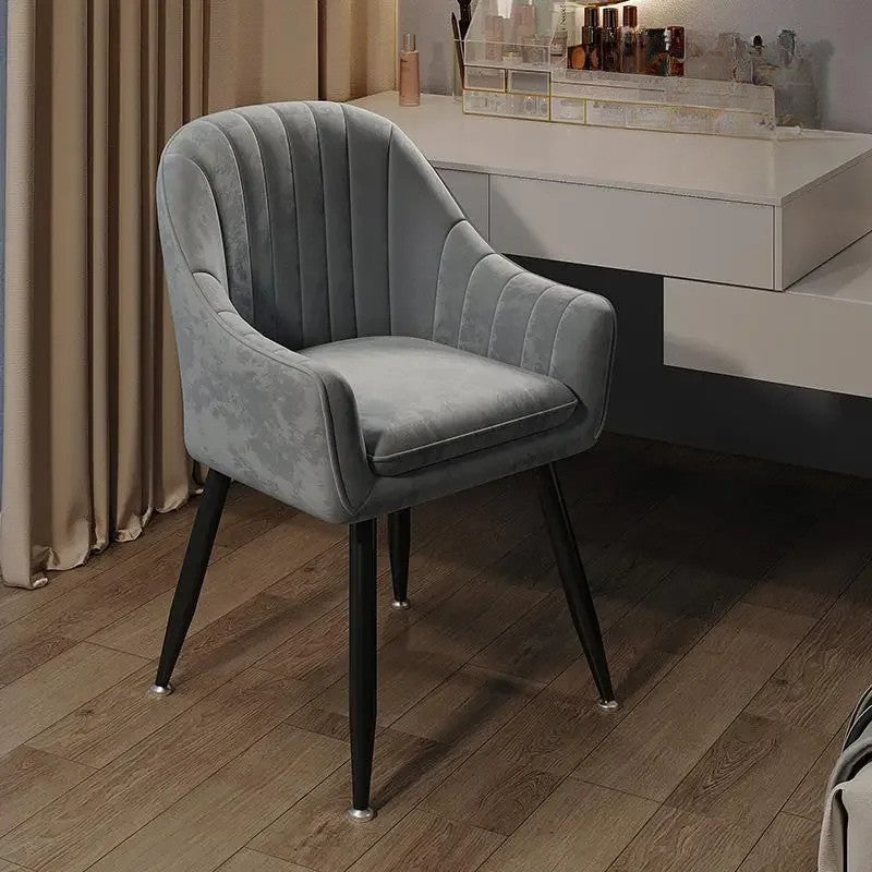 Gray velvet chair in a room with a vanity table and makeup products.