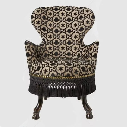Decorative armchair with patterned fabric and black fringe on a white background
