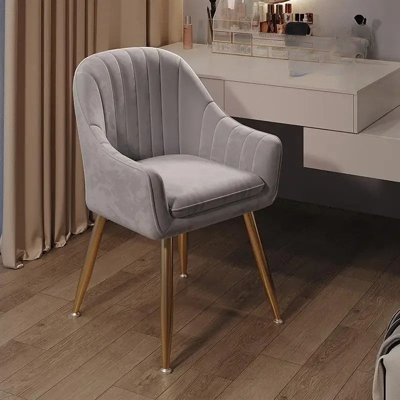 Gray velvet chair with gold legs on a wooden floor in a room setting.