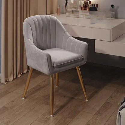 Gray velvet chair with gold legs on a wooden floor in a room setting.